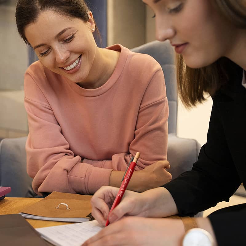 Zwei Frauen schreiben im Büro mit graviertem Alu-Kugelschreiber – ideal für den Alltag